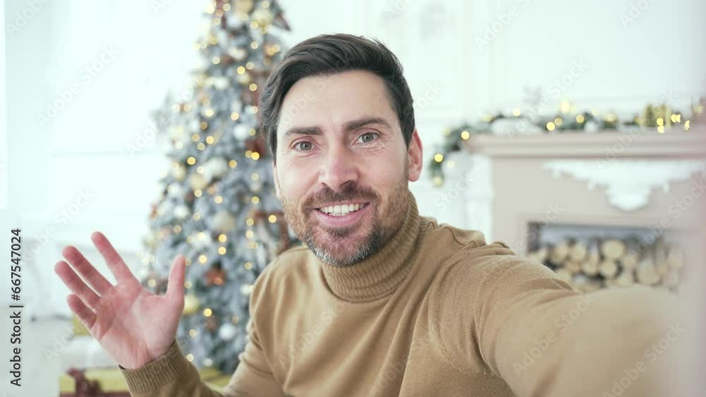 POV Webcam view. Happy handsome man talking on a video call using a smartphone in living room at home during winter New Year Christmas Xmas holidays. Smiling male talking wishes congratulates remotely POV Webcam view. Happy handsome man talking on a video call using a smartphone in living room at home during winter New Year Christmas Xmas holidays. Smiling male talking wishes congratulates remotely
