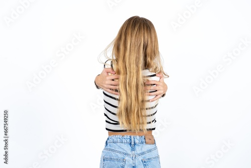 Beautiful caucasian teen girl wearing striped T-shirt hugging herself happy and positive from backwards. Self love and self care