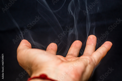 gray smoke comes out with beautiful shapes from a male hand on a black background	
