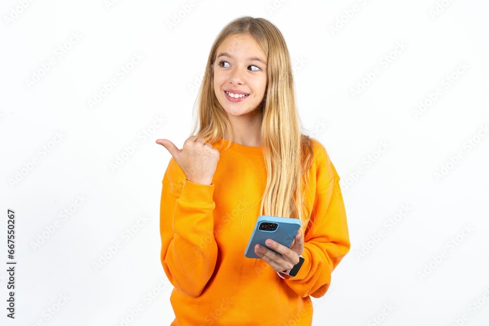 Beautiful teen girl using and texting with smartphone pointing and showing with thumb up to the side with happy face smiling Beautiful teen girl using and texting with smartphone pointing and showing with thumb up to the side with happy face smiling
