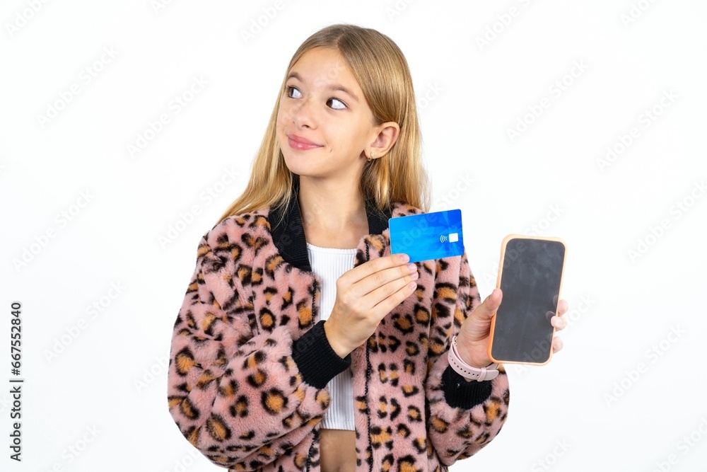 Beautifu blonde kid girl holding bank card modern device looking empty space Beautifu blonde kid girl holding bank card modern device looking empty space