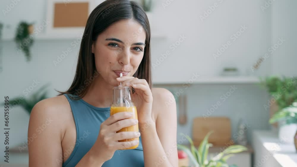 Video of beautiful sporty woman drinking healthy orange juice while standing in the kitchen at home Video of beautiful sporty woman drinking healthy orange juice while standing in the kitchen at home