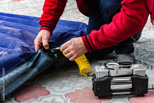 Slika na platnu Man pumps rubber mattress for swimming with car compressor.