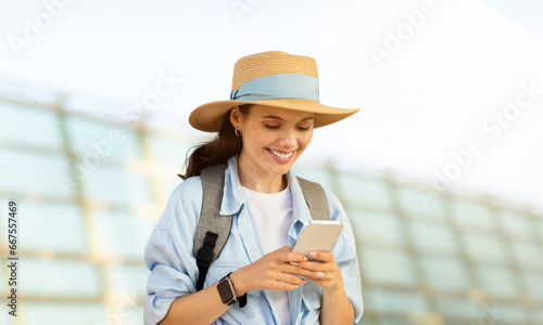 Cheerful millennial caucasian lady tourist in hat with backpack, typing on phone, use online map #667557469