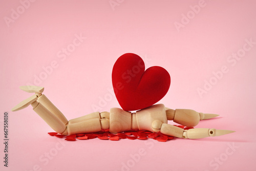 Wooden mannequin lying under heavy heart - Concept of love troubles photo