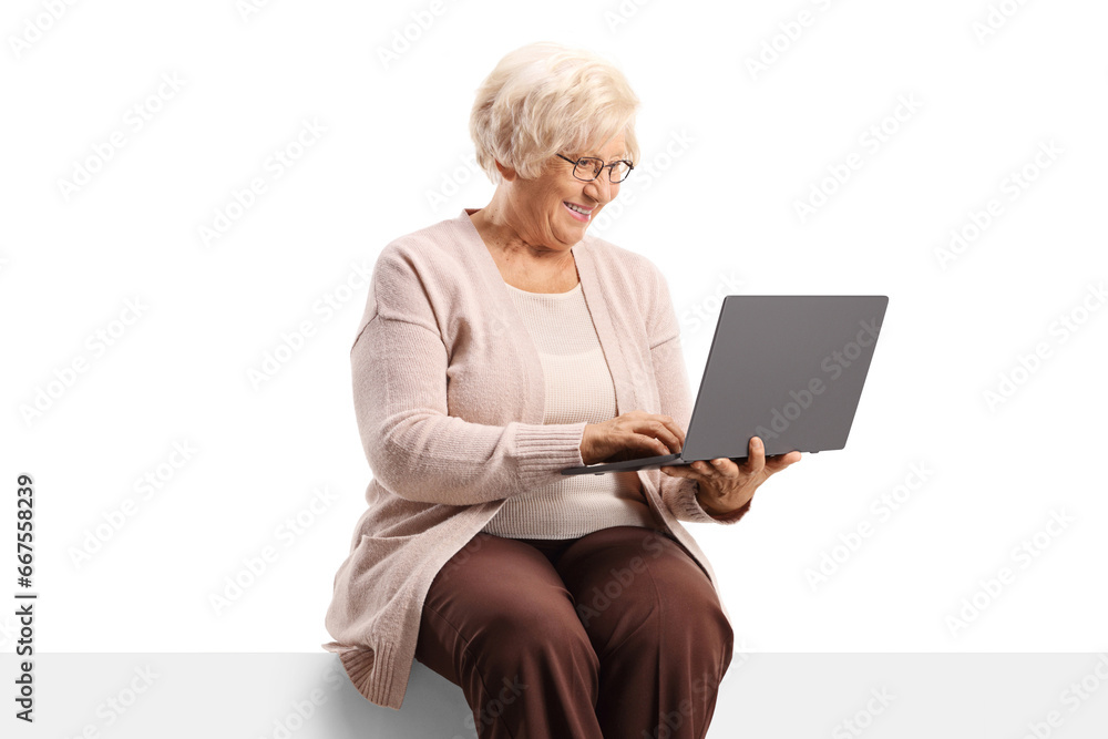 Cheerful elderly woman sitting on a blank panel and using a laptop computer Cheerful elderly woman sitting on a blank panel and using a laptop computer