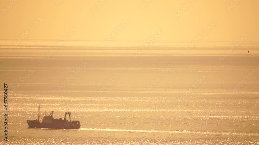 Fishing ship trawler at sunset in the sea. Abstract aerial sea summer ocean sunset nature background. Small waves on calm water surface in motion blur with golden bokeh lights from sun. Fishing ship trawler at sunset in the sea. Abstract aerial sea summer ocean sunset nature background. Small waves on calm water surface in motion blur with golden bokeh lights from sun.