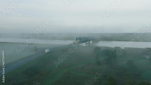 Aerial establishing view of the steel bridge over Lielupe river (Latvia) on a sunny summer morning, fog rising over the river, cars driving, wide drone shot moving forward low photo