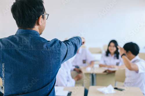 Asian male teacher angry and pointing at noisy students in classroom