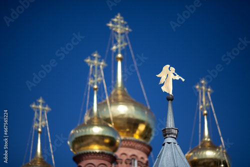 Gilded angel shaped weathervane on the steeple, blurred golden domes and crosses and blue sky on background; Chernigovsky Skit, Sergiev Posad, Russia.