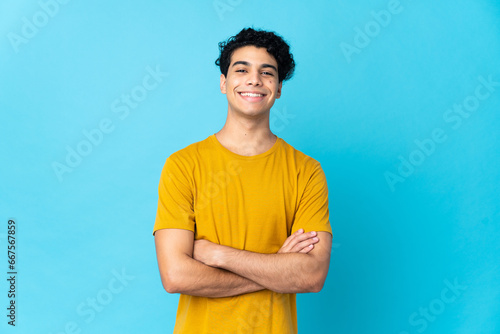 Young Venezuelan man isolated on blue background keeping the arms crossed in frontal position