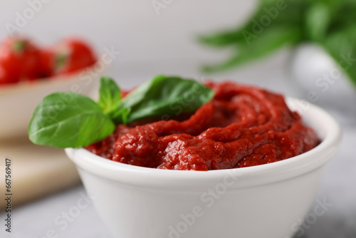 Tasty tomato paste and basil in bowl on table, closeup