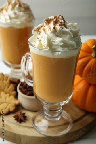 Tasty pumpkin latte with whipped cream in glasses, spices and cookies on white table, closeup