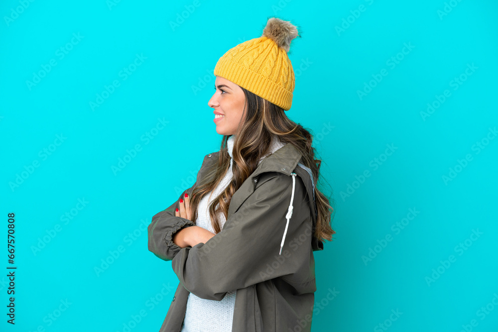 Young Italian woman wearing winter jacket and hat isolated on blue background in lateral position Young Italian woman wearing winter jacket and hat isolated on blue background in lateral position