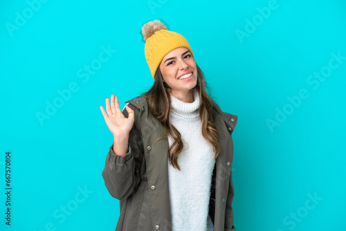 Young Italian woman wearing winter jacket and hat isolated on blue background saluting with hand with happy expression photo