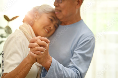 Shot of elderly couple spouses dancing in living room and looks at each other with love