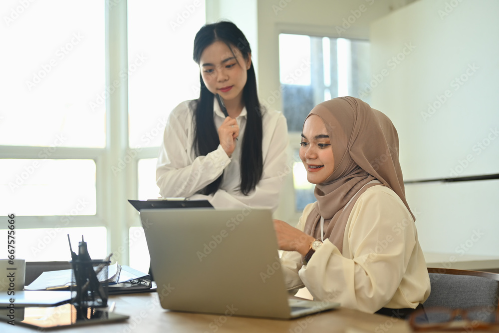 Smiling young Muslim businesswoman using laptop and checking financial document with her colleagues Smiling young Muslim businesswoman using laptop and checking financial document with her colleagues