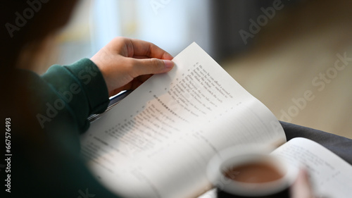 Closeup view of young woman drinking coffee and reading book on couch at home