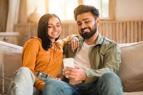 Happy Indian couple on sofa, sharing a joyful moment with smartphone