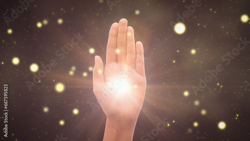 Visualization Of Male Or Female Hand Reaching Out To Show Hamsa Religious Gesture on Magical Dark Background. Bright Light Glowing In The Middle Of Palm. Traditional Protection Sign Concept.