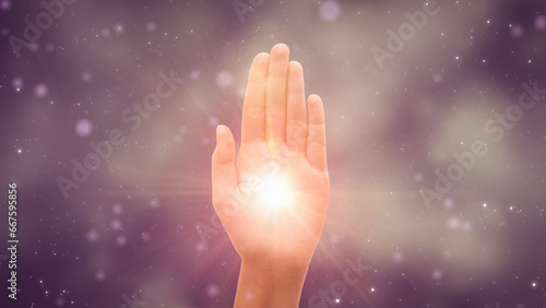 Visualization Of Male Or Female Hand Reaching Out To Show Hamsa Religious Gesture on Dark Purple Background. Bright Light Glowing In The Middle Of Palm. Traditional Protection Sign Concept.