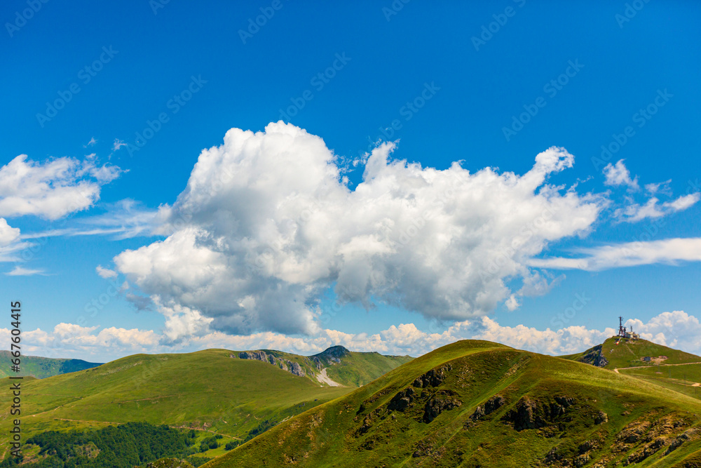A massive white cloud over green hills and gray cliffs, a breathtaking natural contrast