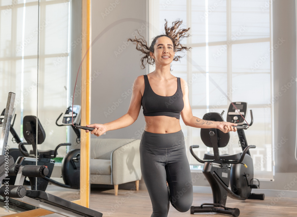 Fototapeta premium Sportswoman training using skipping rope in gym of sports, health care. jumping rope behind punching bags in gym