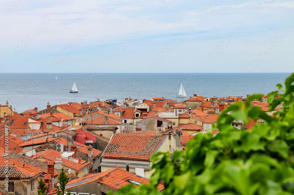 Panoramic Mediterranean view of red tiled roofs and blue sea with white sailboats