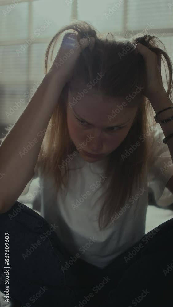 Vertical shot of depressed girl sitting at home and pulling her hair while experiencing anxiety and stress Vertical shot of depressed girl sitting at home and pulling her hair while experiencing anxiety and stress