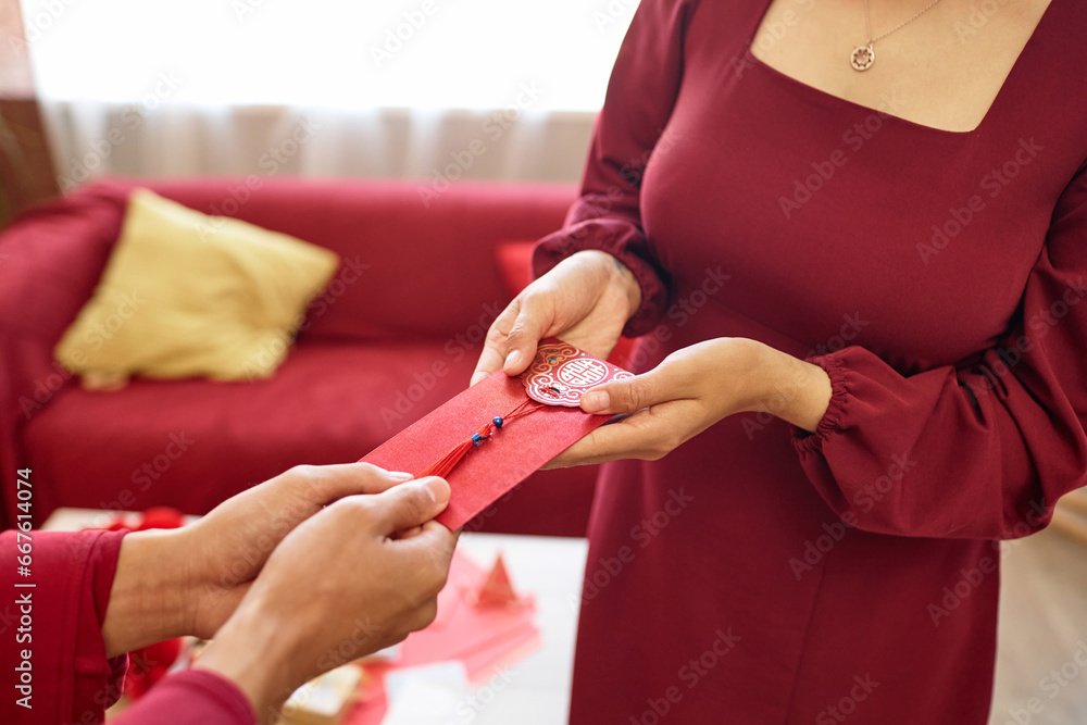 Closeup of Asian young couple exchanging gifts and ornate red envelopes as Chinese New Year tradition for good fortune, copy space
