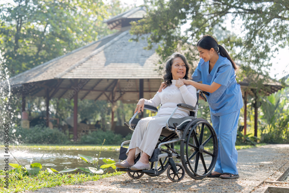 Young female in uniform with senior patient in a wheelchair chilling out in park Young female in uniform with senior patient in a wheelchair chilling out in park