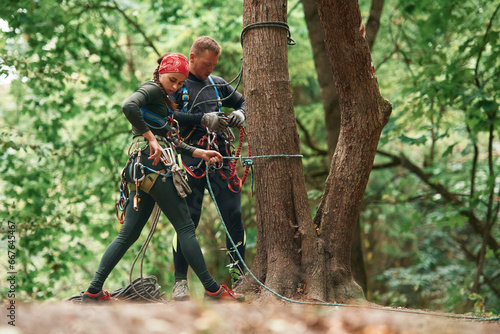 Setting up the ropes. Man and woman doing climbing in forest with use of safety equipment
