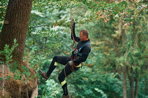 Hanging on a rope. Man is doing climbing in the forest by use of safety equipment