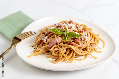 Spaghetti carbonara with cheese and basil on white plate with golden fork on white marble background,