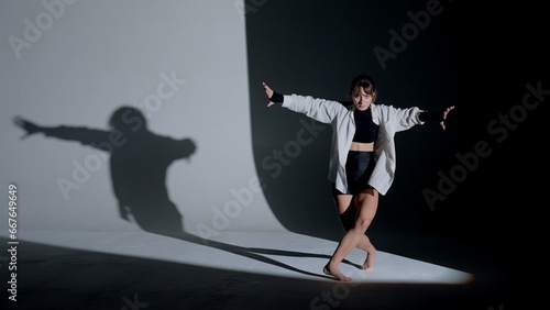 Wallpaper Mural Young woman wearing a top, shorts and a shirt performing contemporary dance under a spotlight in the studio. Contrasting black falling shadow on the background. Full length. Torontodigital.ca