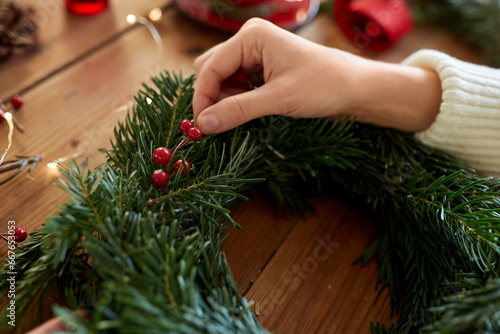 winter holidays, diy and hobby concept - close up of woman with berry decorations making fir christmas wreath at home