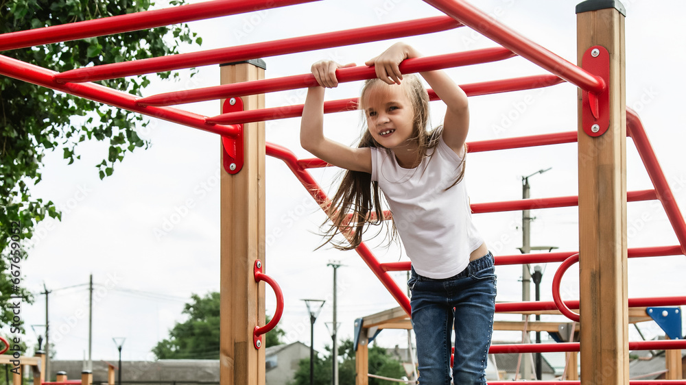 Child girl plays on a street playground. girl is hanging on a horizontal bar. the concept of a healthy lifestyle. happy childhood.