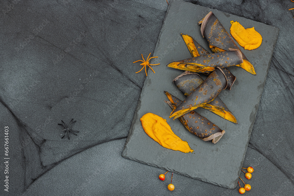 Halloween sweet dessert with traditional decor. Thin black pancakes with pumpkin cream, fall leaves