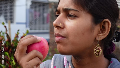 Happy young girl biting an apple at home. Beautiful Asian young woman eating fresh apple fruit outdoors. Healthy fresh food and vegetarian dieting concept. 4k video. photo