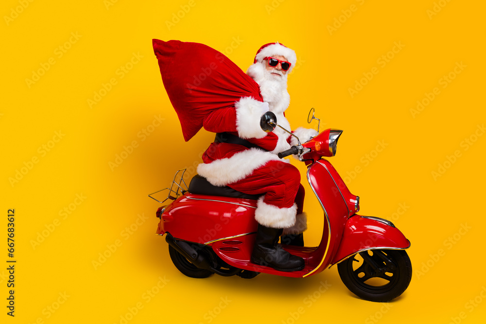 Side photo of confident driving transport motorbike wear red santa claus costume grandfather hold sack isolated on yellow color background Side photo of confident driving transport motorbike wear red santa claus costume grandfather hold sack isolated on yellow color background