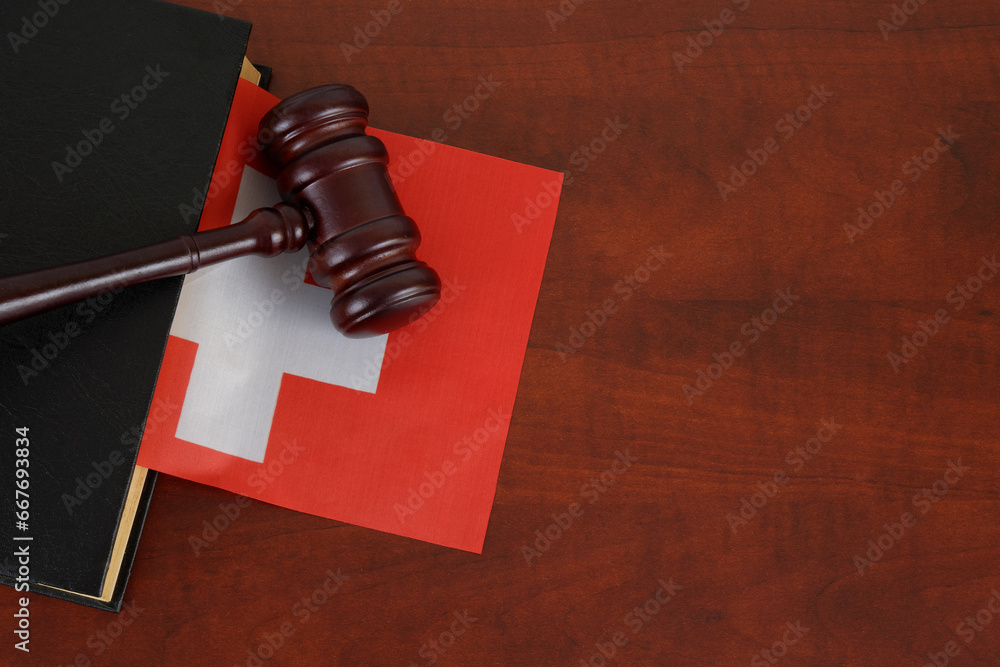 Gavel and legal book on wooden table with flag of Switzerland. Copy space for text.
