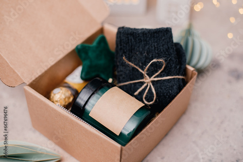 Obraz na plátně Christmas box with presents - candle in dark jar, chocolate candies, cozy grey socks and festive decoration