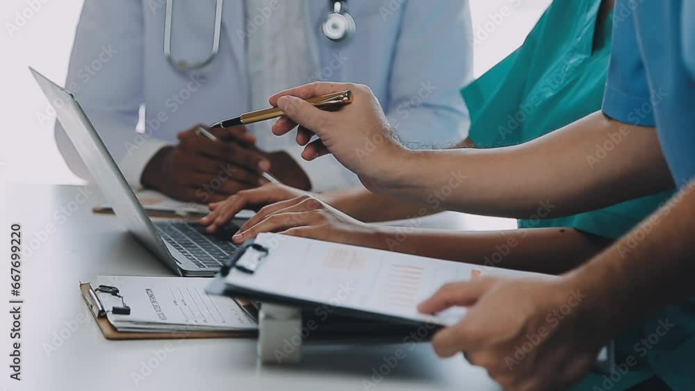 Multiracial medical team having a meeting with doctors in white lab coats and surgical scrubs seated at a table discussing a patients records Multiracial medical team having a meeting with doctors in white lab coats and surgical scrubs seated at a table discussing a patients records