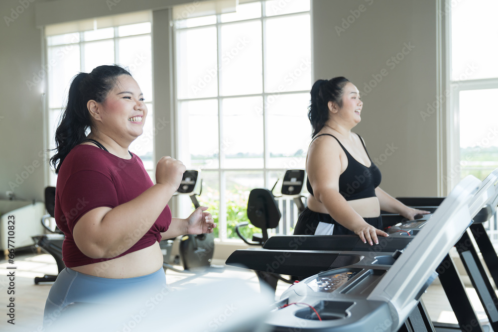 Two Asian young chubby size women running on treadmill in fitness club. Young overweight women exercise on treadmill in gym together Two Asian young chubby size women running on treadmill in fitness club. Young overweight women exercise on treadmill in gym together