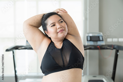 Happy Asian young chubby size woman in sportswear stretching body in fitness club. Young overweight woman warm up before workout at gym. Workout sport concept