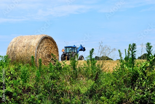 Tractor at farm moving bales of hay .