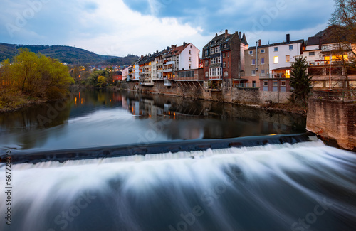 Panoramic view of Hagen-Hohenlimburg, Germany. Row of old houses with balconys and verandas above a casacade of the Lenne river with reflection at evening blue hour with lights and longtime exposure. photo