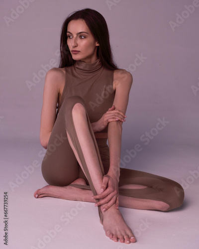 A beautiful young girl in a grey bodysuit sits on a light background.