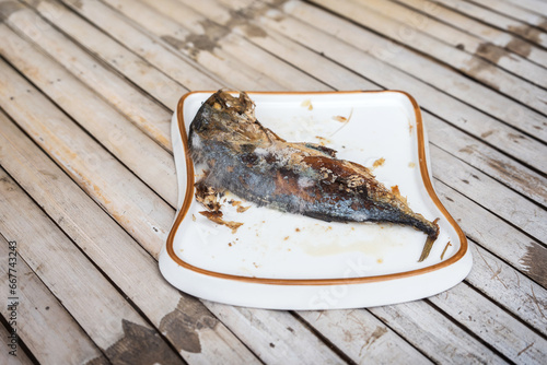 The food waste. Remains of fried fish. Fried mackerel that was forgotten on the table was spoiled and moldy in a white plate the shape of bread. photo