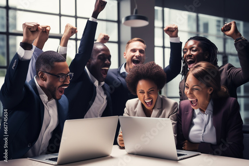 Group of overjoyed multiracial business people with fists up in the air, , screaming loud and celebrating company success while they are gathered around table with laptop in the office.